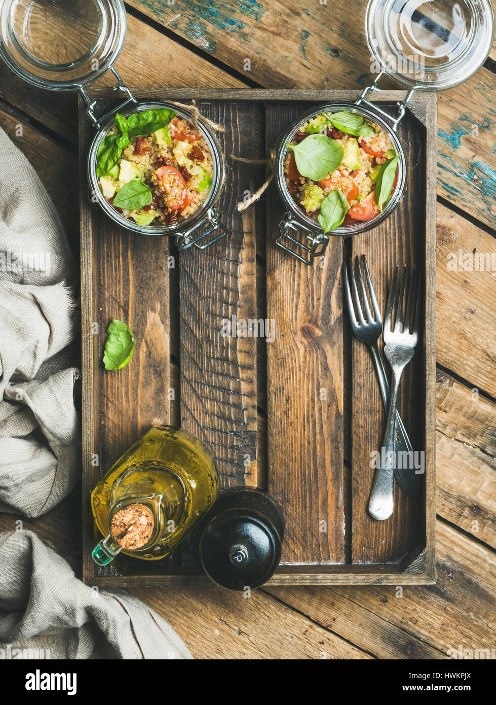 Homemade healthy jar quinoa salad with cherry and sun-dried tomatoes, avocado, basil in wooden box over rustic background, top view, copy space. Detox Stock Photo