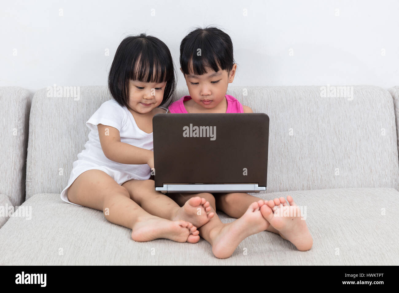 Asian Chinese little sisters playing computer on the sofa in the living ...
