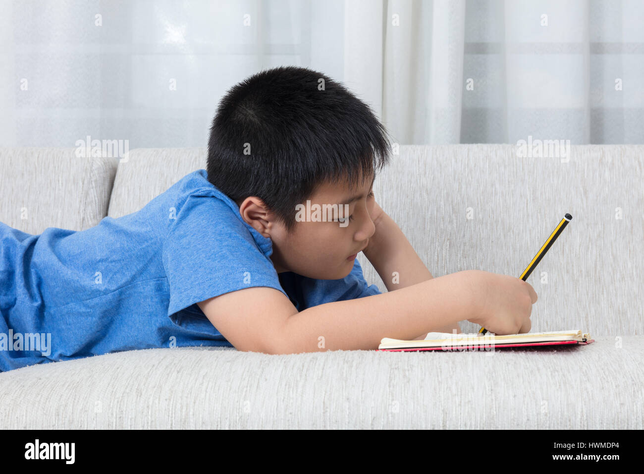 Bored Asian Chinese little boy writing book on the sofa in the living