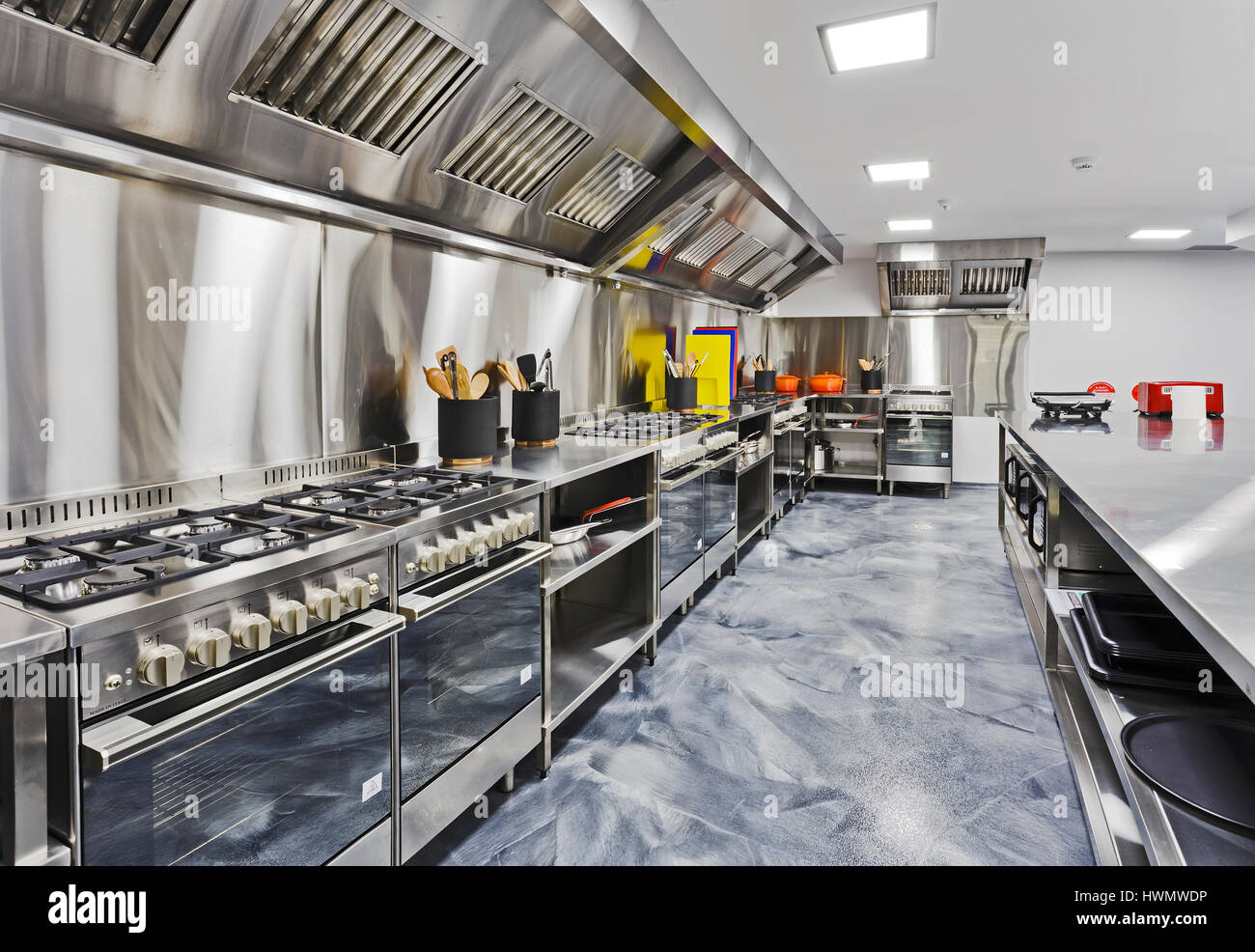 Modern shiny kitchen with stainless still kitchenware and equipment for restaurant-scale cooking with preparation tables, pans, pots, stoves. Stock Photo