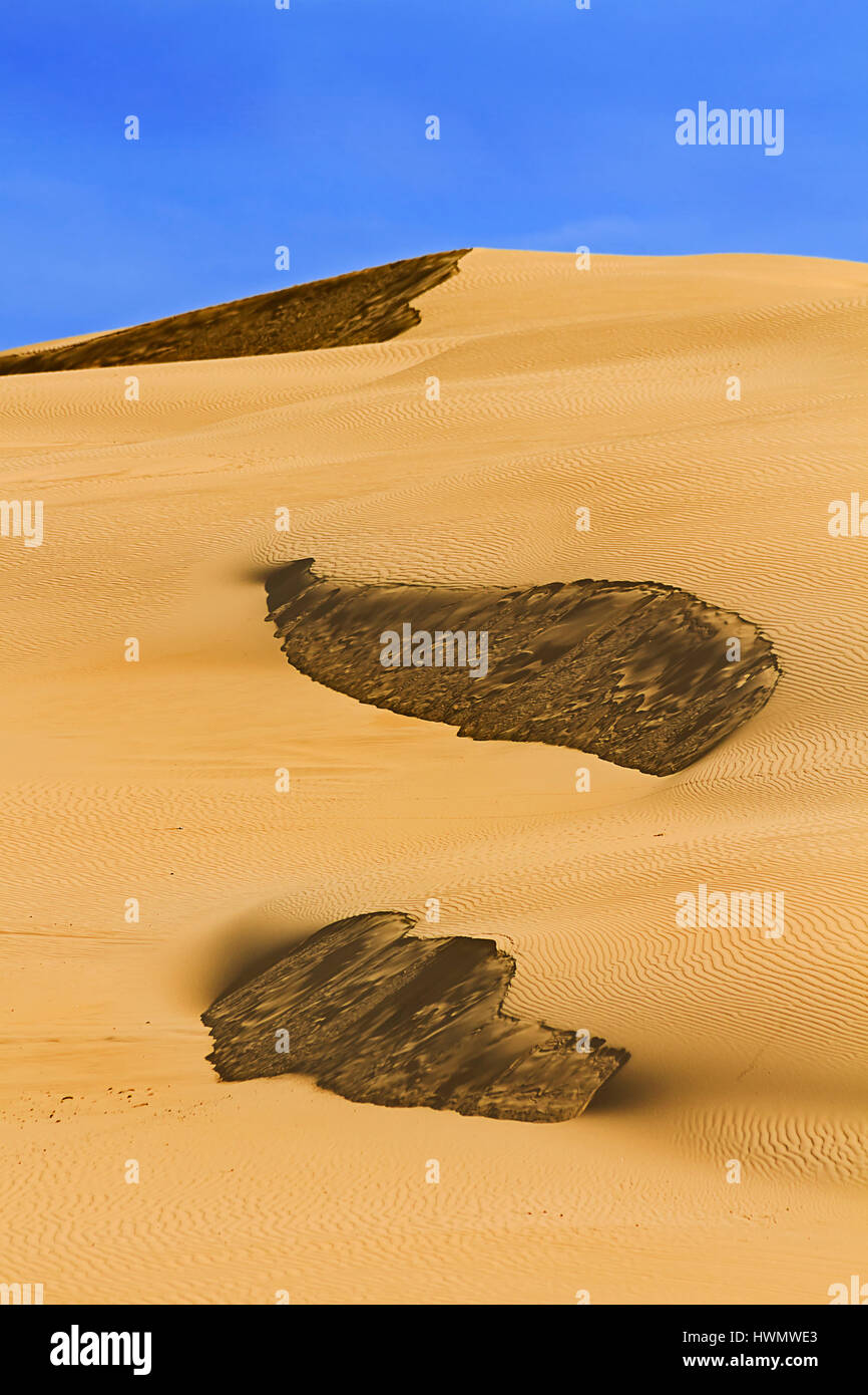 Untouched sand dunes of desert like landstape under blue sky. Dark spots on sand dunes sides part of natural texture and structure of sand. Stock Photo
