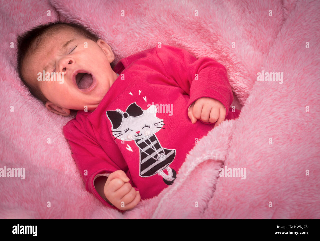 A newborn baby girl yawning on a pink blanket, certainly gazed lovingly by her parents who take advantage of the slightest of her comical expressions. Stock Photo