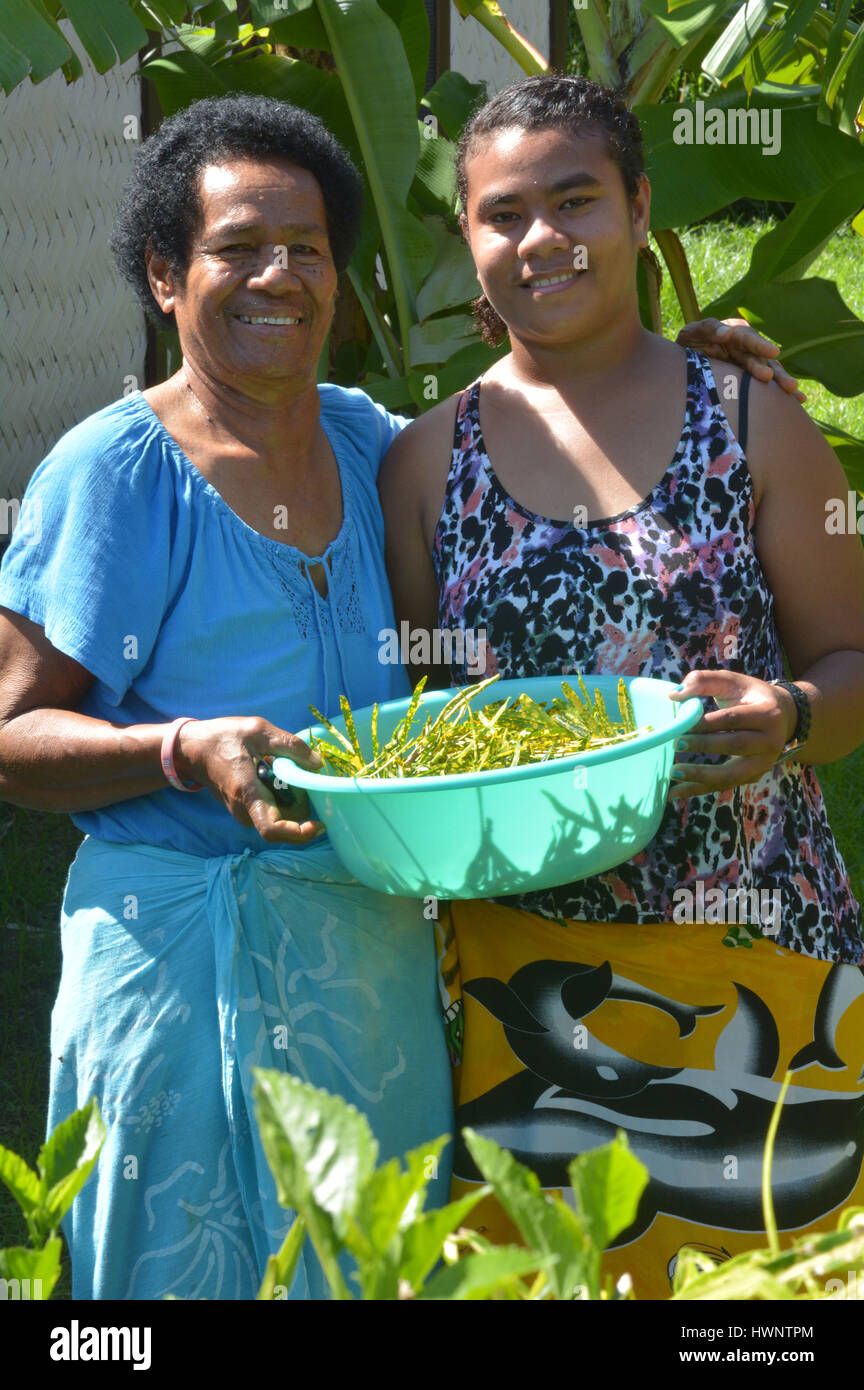 Indigenous Fijian mother and daughter collect together vegetables in the home garden. Stock Photo