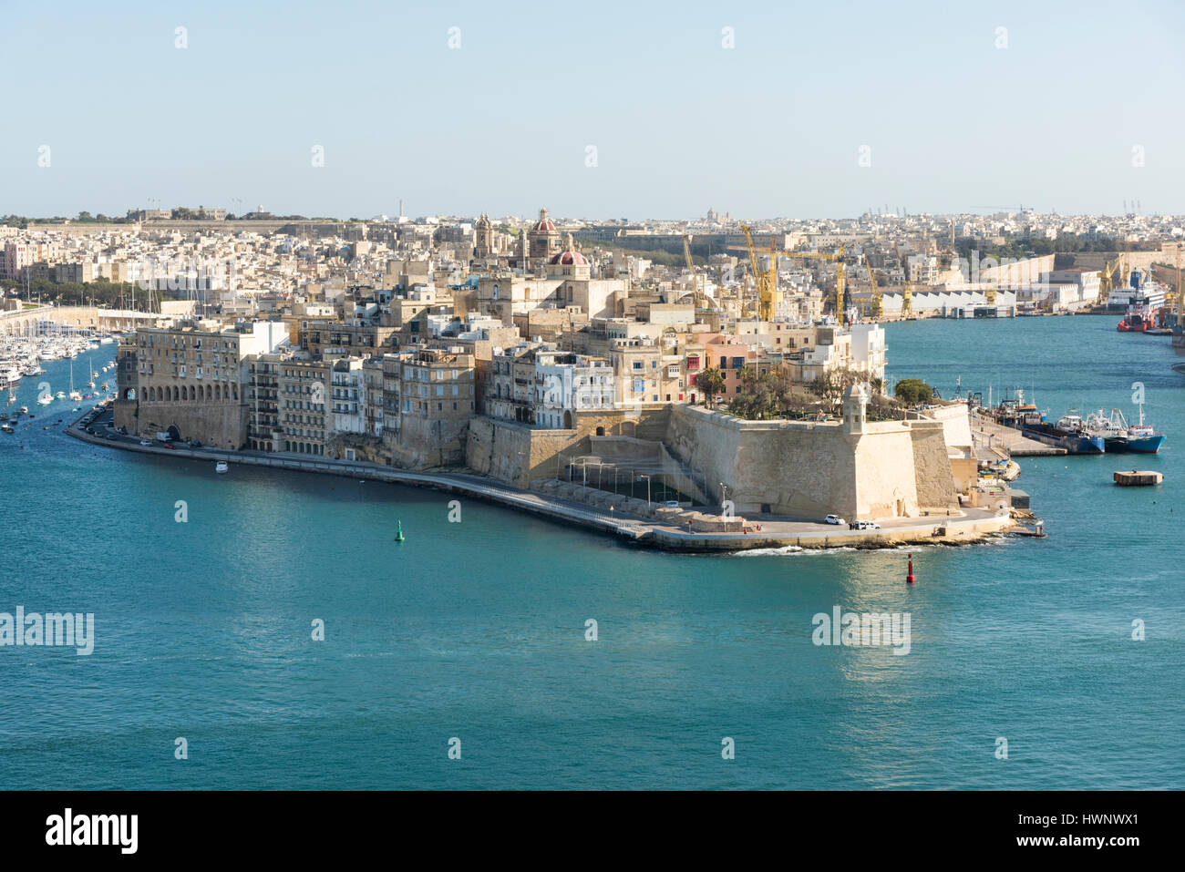 A view into the Grand Harbour from Valetta to the Three Cities with old buildings and moored boats at Vittoriosa Malta Stock Photo