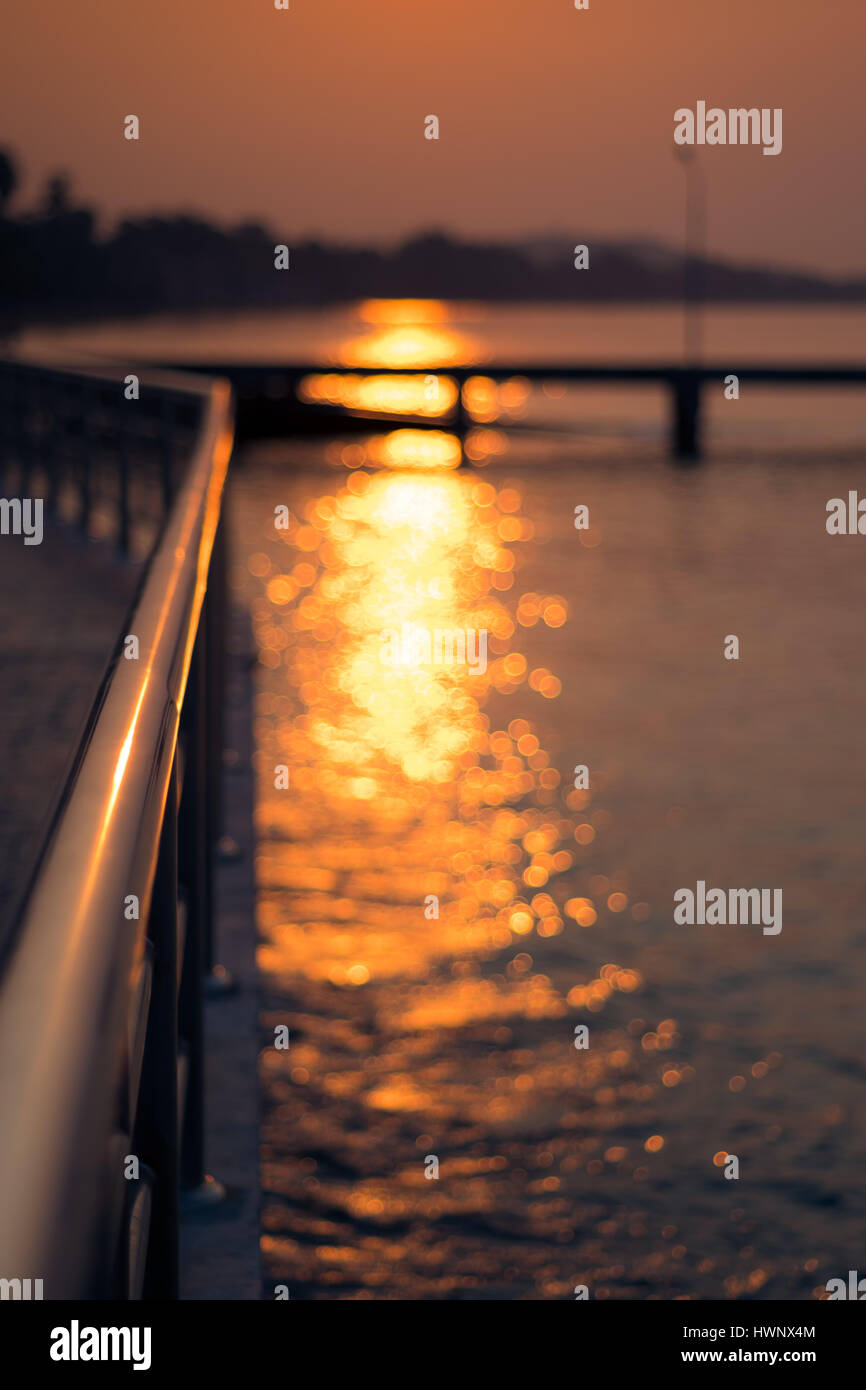 Sunlight with bokeh on water next to metal rail by the sea in Sattahip, Thailand. Stock Photo
