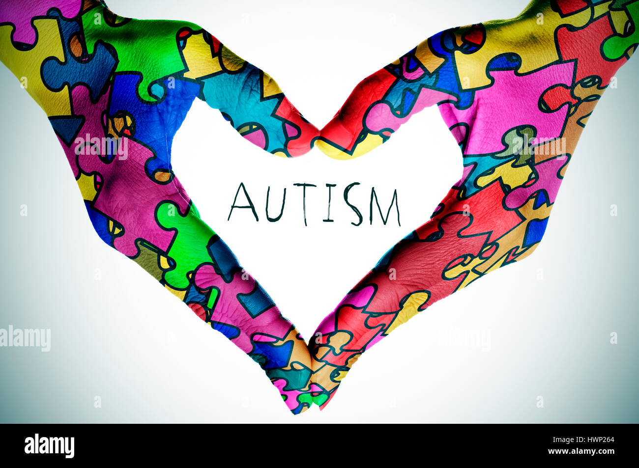 woman hands forming a heart patterned with many puzzle pieces of different colors, symbol of the autism awareness, and the text autism, with a slight  Stock Photo