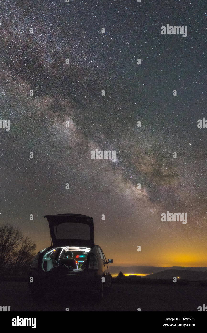 A lone star gazer rests on the hood of a car with the inside lit, looking up at the Milky Way over the mountains of West Virginia. Stock Photo