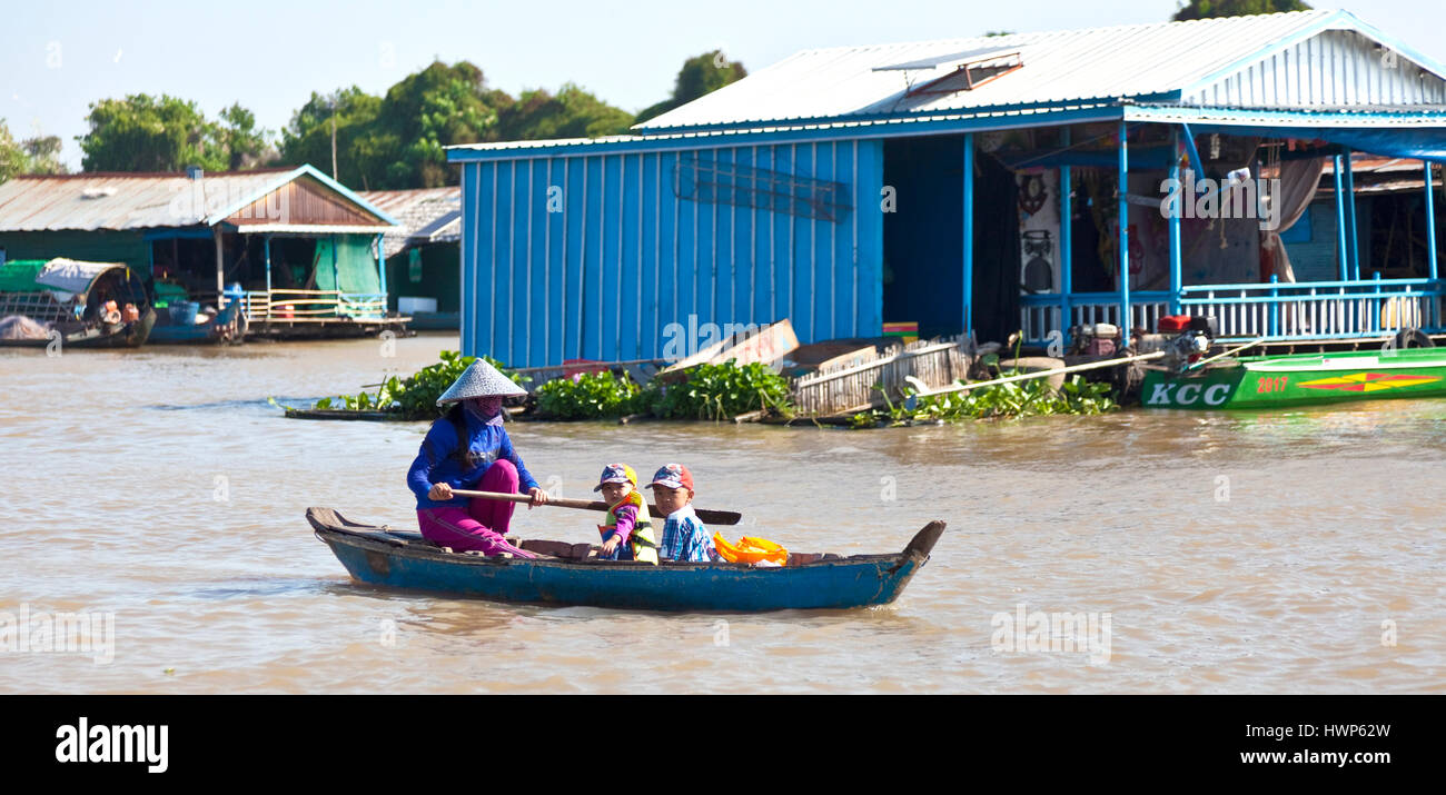 Cambodian woman uses oar to propel her children by boat to school at Kampong Chhnang Stock Photo