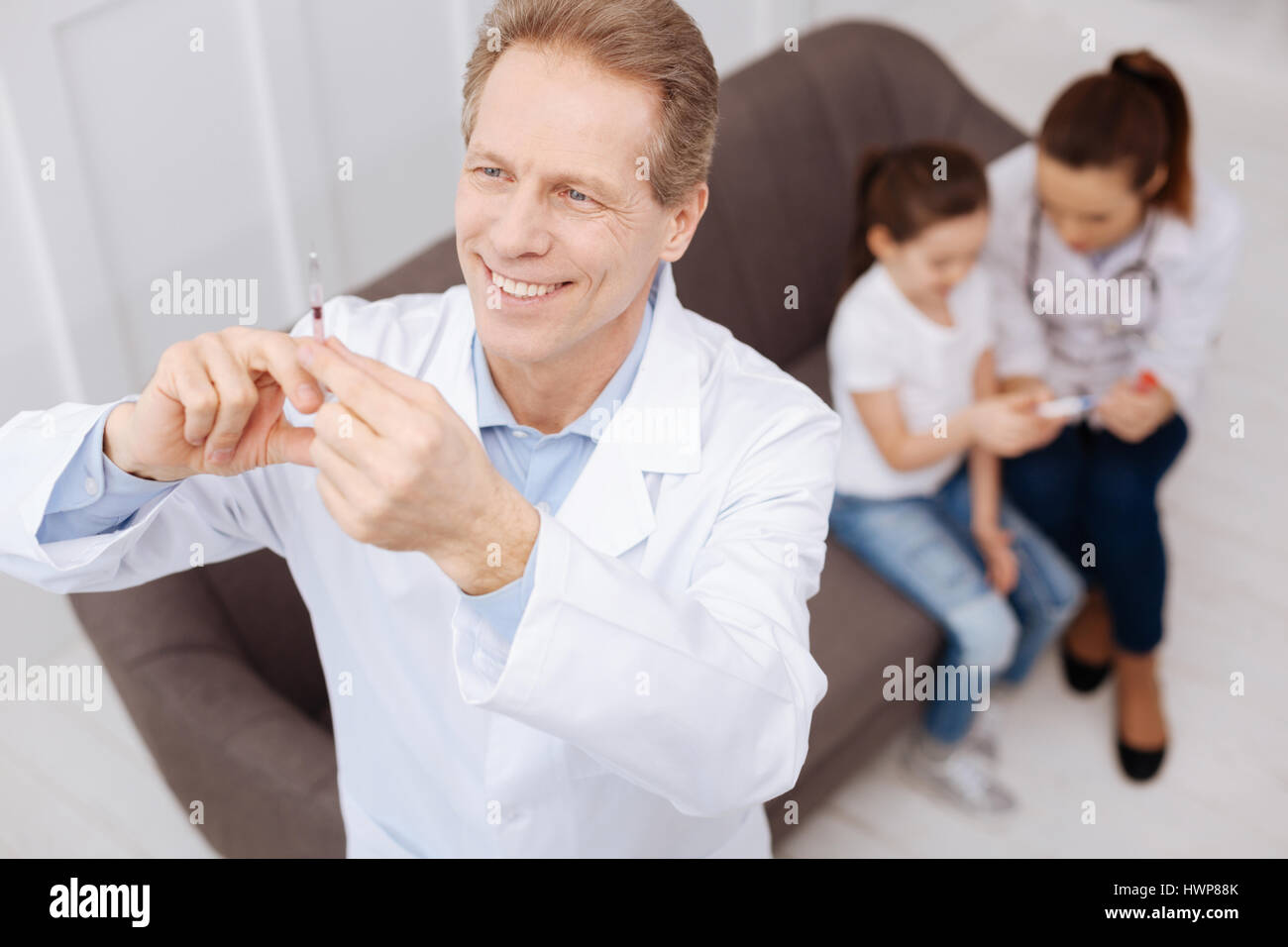 Great remedy. Focused energetic prominent doctor preparing a flu vaccine for his little patient while his colleague comforting her and checking her te Stock Photo