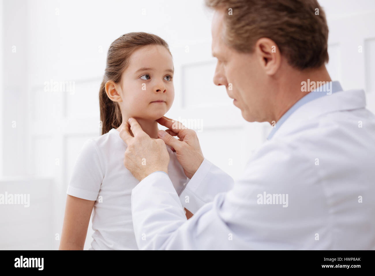 Does it hurt. Determined gentle prominent doctor examining little girls glands while comparing her symptoms to diagnosis Stock Photo