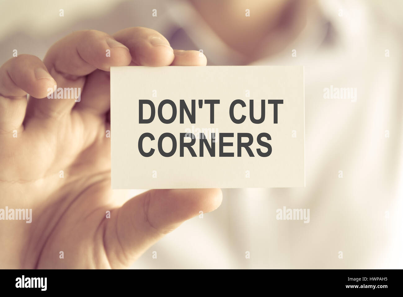 Closeup on businessman holding a card with text DONT CUT CORNERS ...