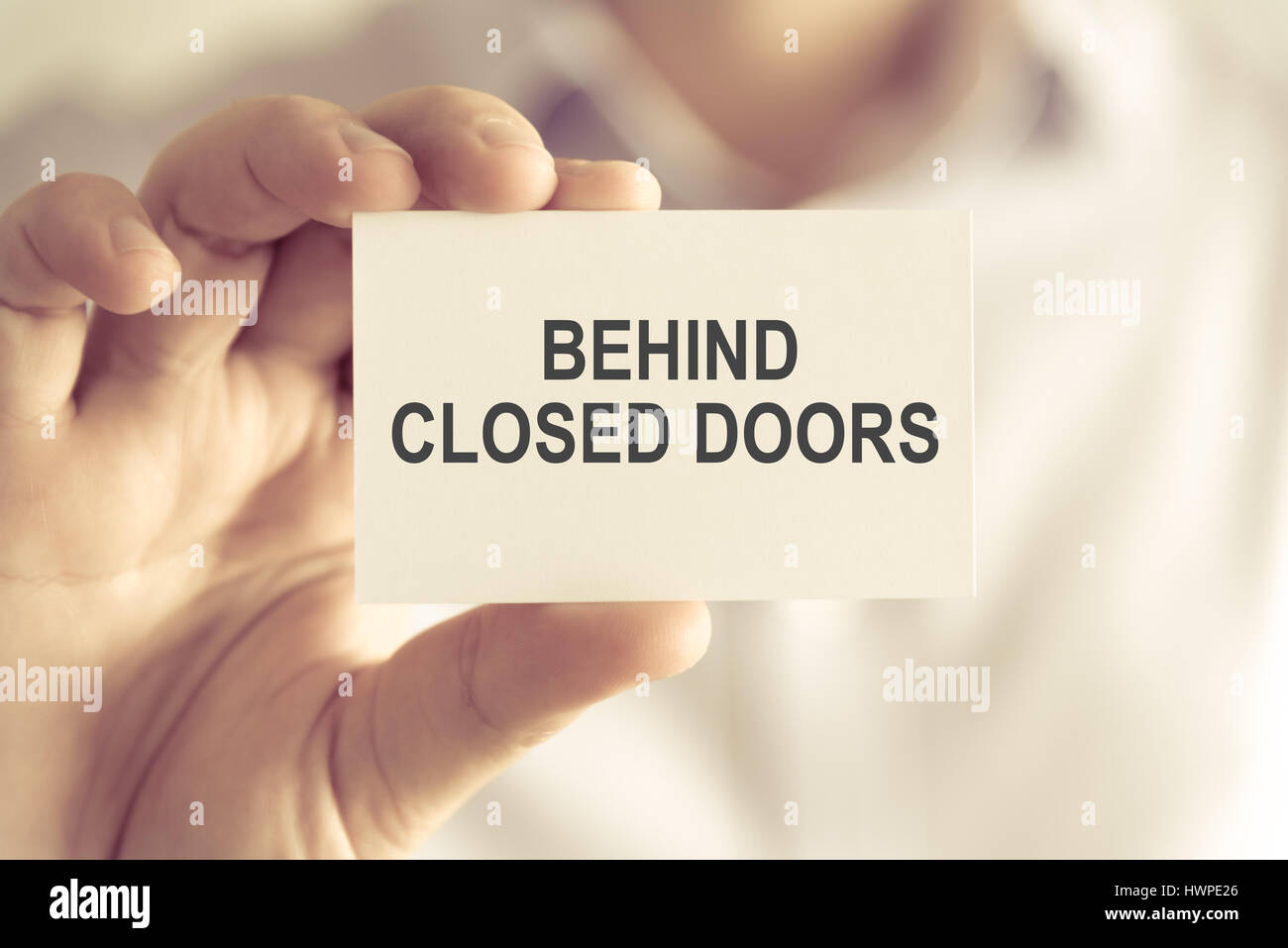 Closeup on businessman holding a card with text BEHIND CLOSED DOORS, business concept image with soft focus background and vintage tone Stock Photo