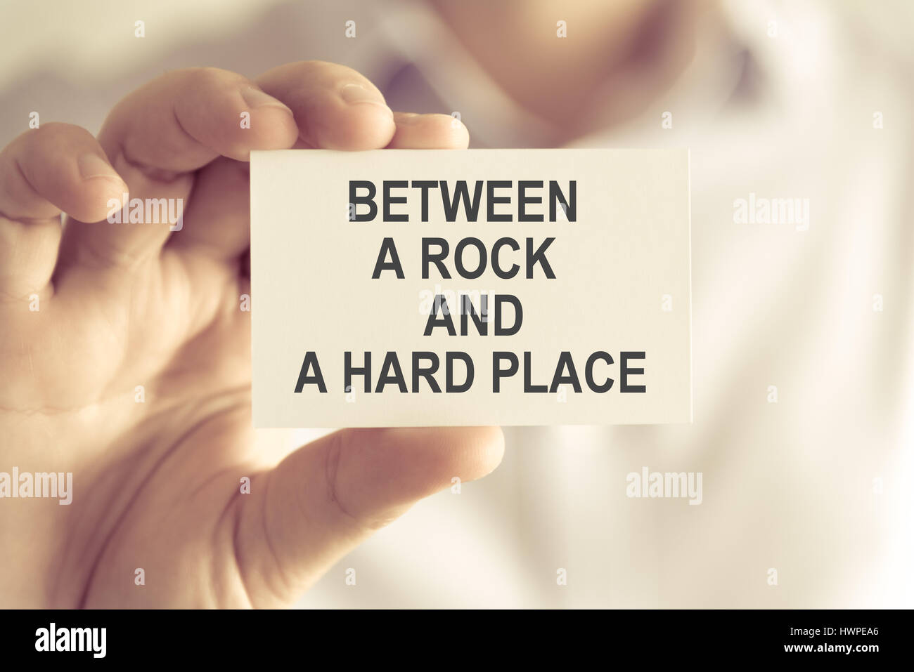 Closeup on businessman holding a card with text BETWEEN A ROCK AND A ...