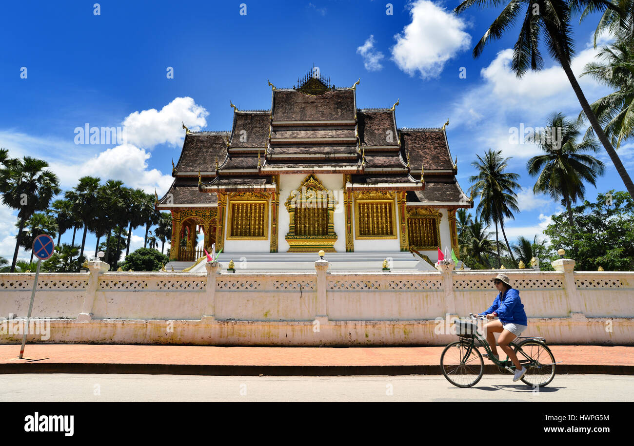 Loungprabang,Laos - August 7,2015: Buddhist Temple at Loungprabang royal palace and unfocus of unidentified woman cycling on the main street of the ci Stock Photo