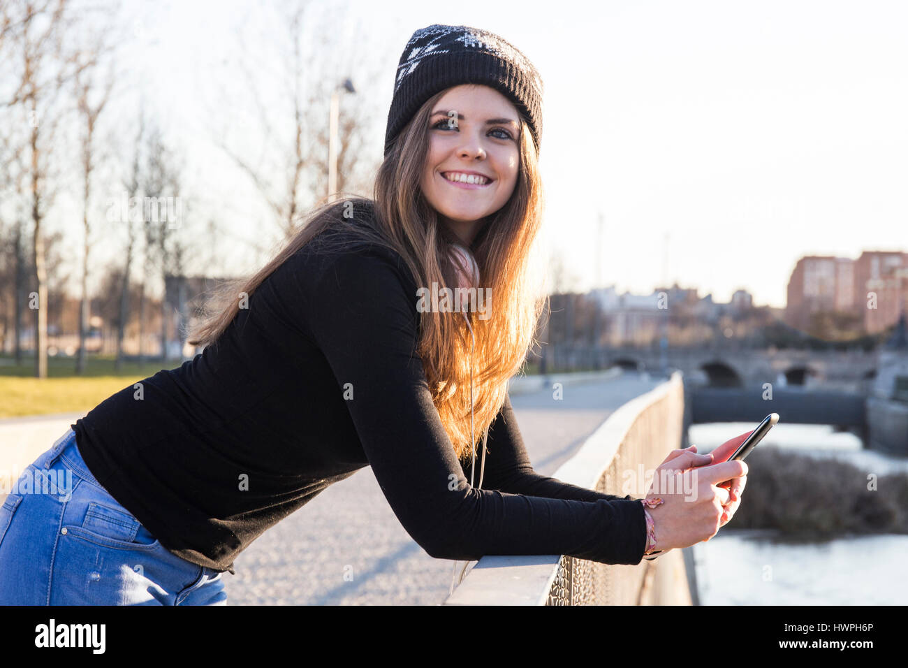 Smiling woman looking away while using mobile phone by river in city Stock Photo