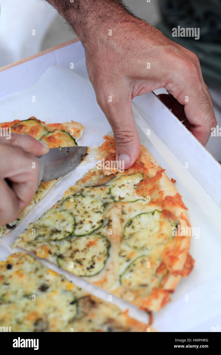 Closeup of male's hand  cutting a slice of vegetarian pizza with a sharp knife. Stock Photo