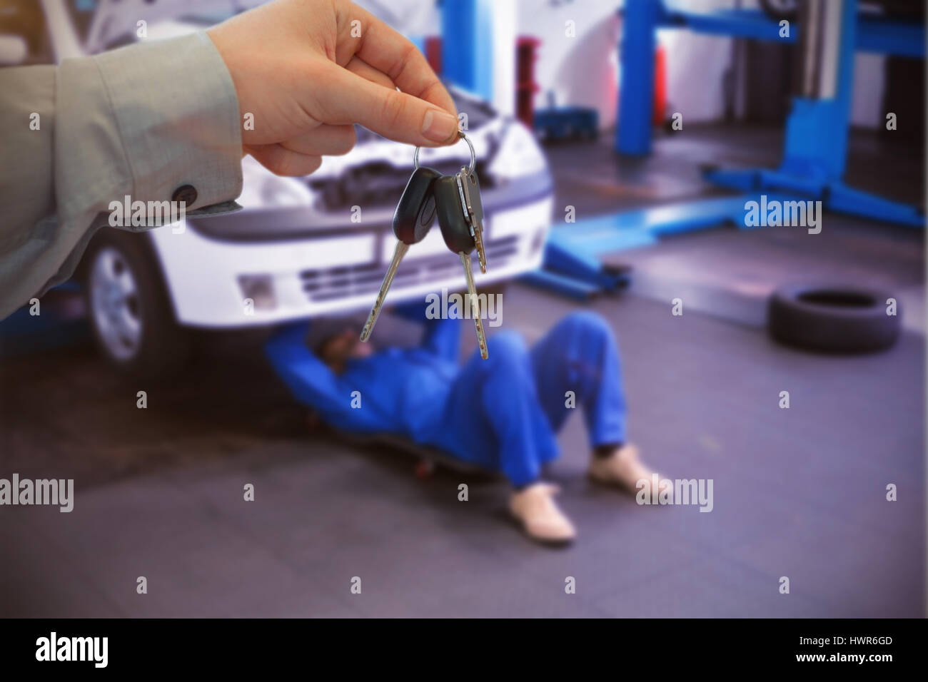 Car dealer giving keys to a customer against mechanic lying and working