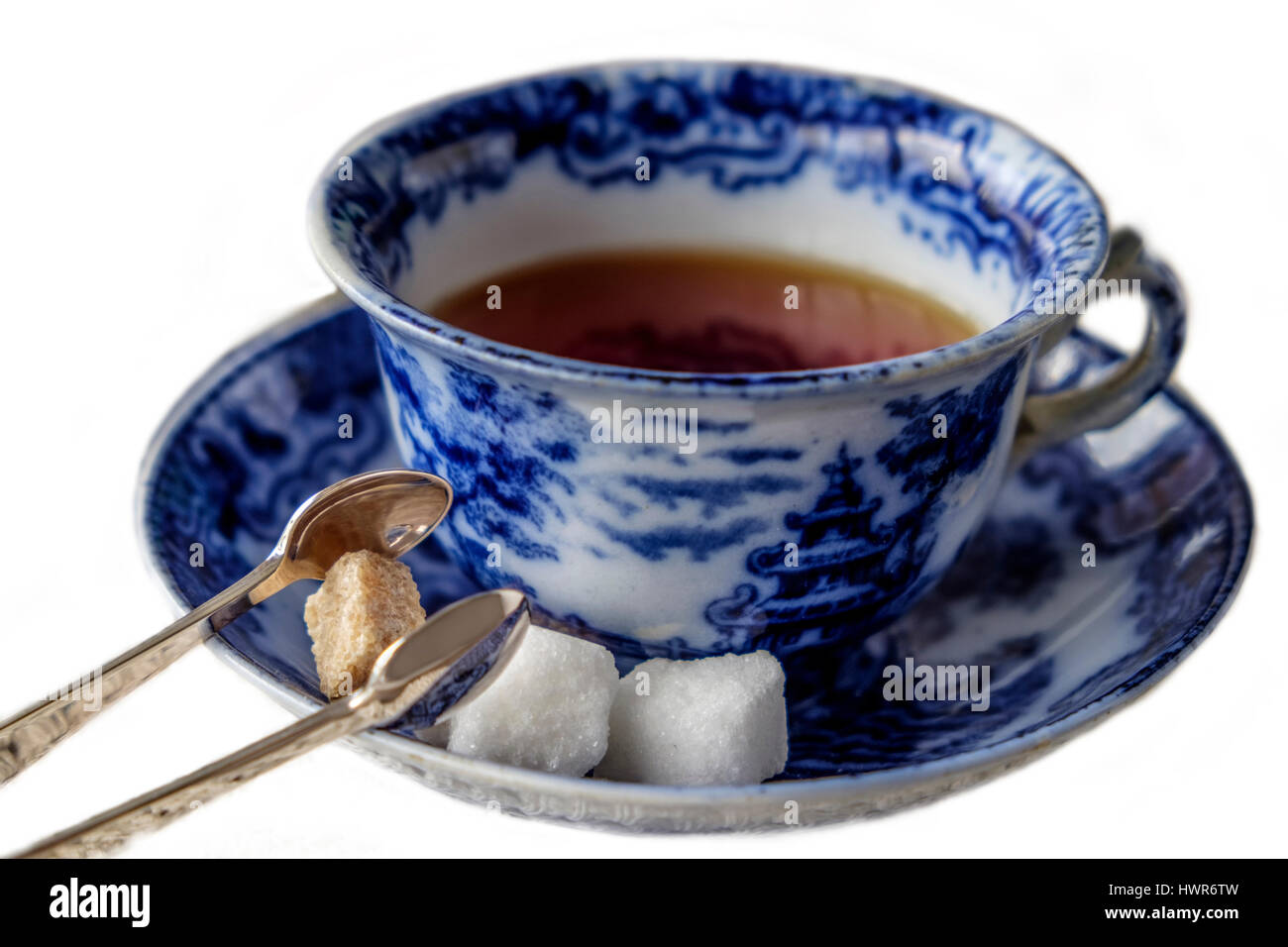 Antique blue and white china cup and saucer of black English breakfast tea with silver tongs for white and brown sugar cubes. Isolated on white backgr Stock Photo