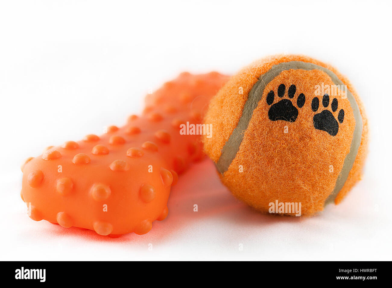 Orange dog toys on a white surface. Bright tennis ball with paw prints