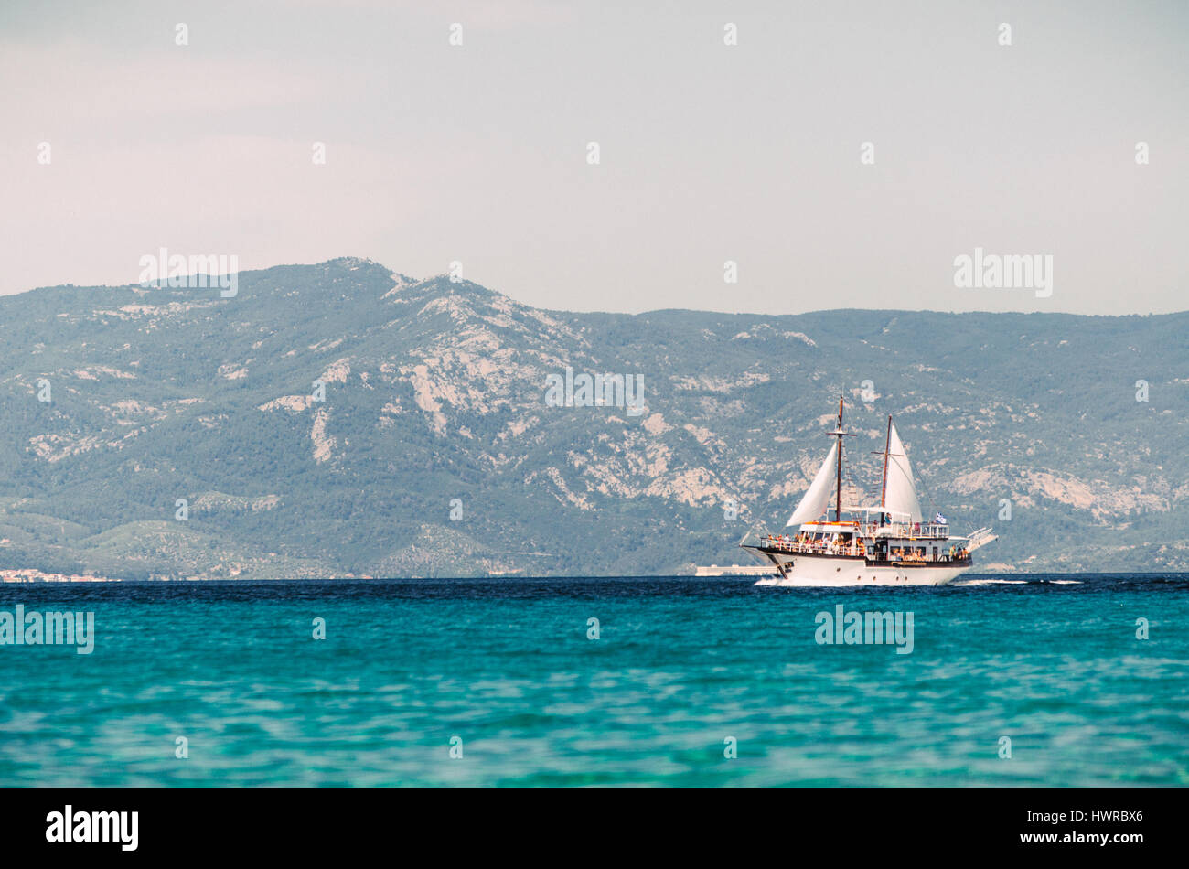 PEFKOHORI, GREECE - MAY 26, 2015: Sailing ship sails in the Aegean Sea on the background of mountains and hills of the peninsula Sithonia, Halkidiki. Stock Photo