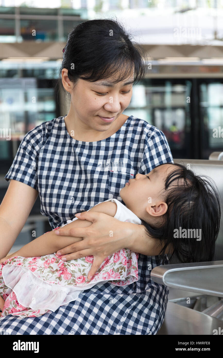 Asian Chinese mother carrying sleeping daughter inside a MRT station in Kuala Lumpur City, Malaysia. Stock Photo