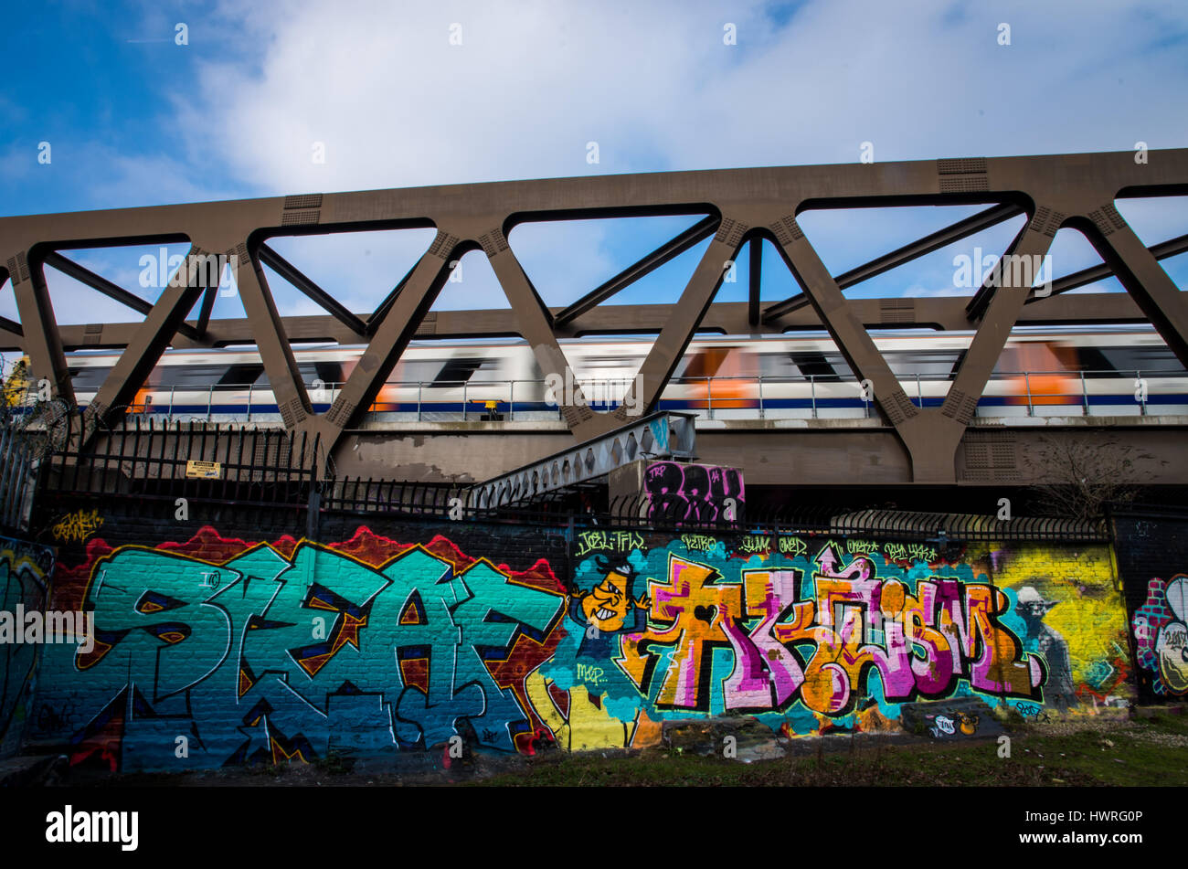 An overground train run fast while crossing a bridge near Bricklane nomadic community where the wall are full of artistic graffiti Stock Photo