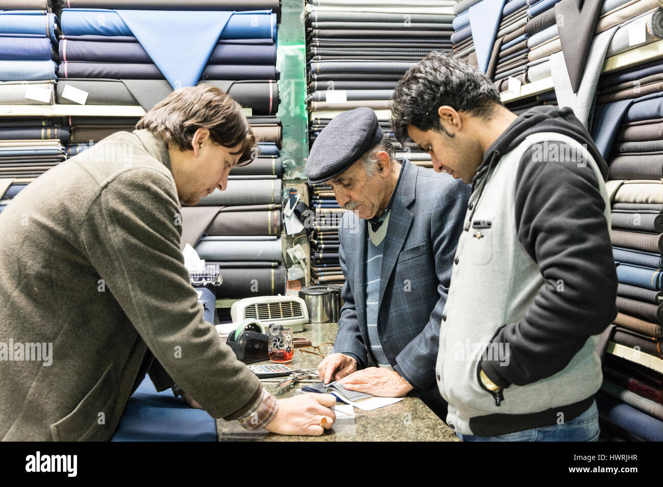 Salesmen and customer surrounded by bolts of wool cloth at fabric stall in the Tehran Bazaar Stock Photo