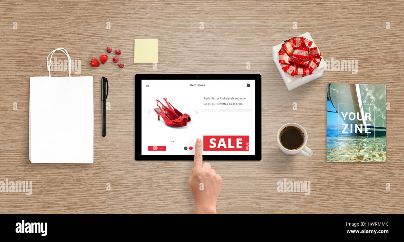 Shopping with tablet. Woman buy red shoes online. Shopping bag for mockup beside. Top view of desk wth gift box, magazine, coffee, pencil, note. Stock Photo