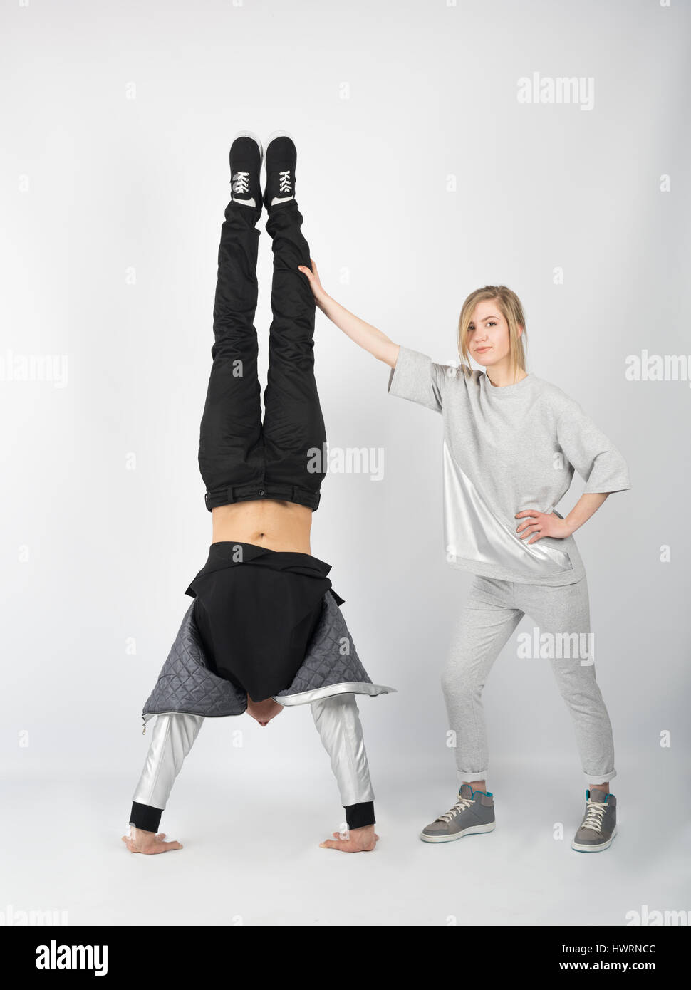 Cheerful couple having fun posing in studio. He stands on his hands and she arched her body and lifted her leg upward. Stock Photo
