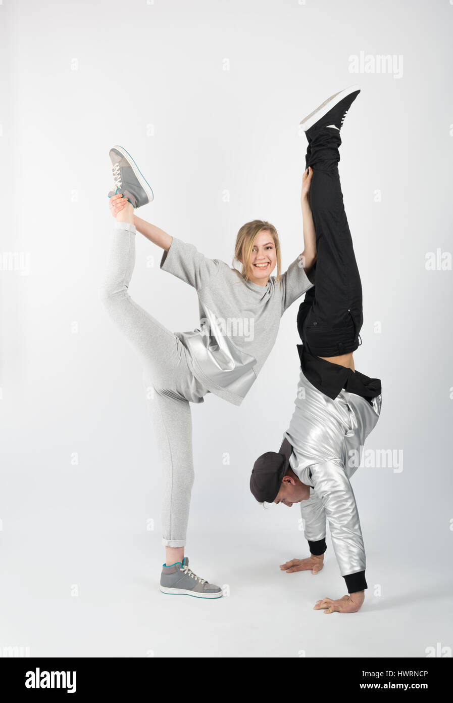 Cheerful couple having fun posing in studio. He stands on his hands and she arched her body and lifted her leg upward. Flexibility and stretching Stock Photo