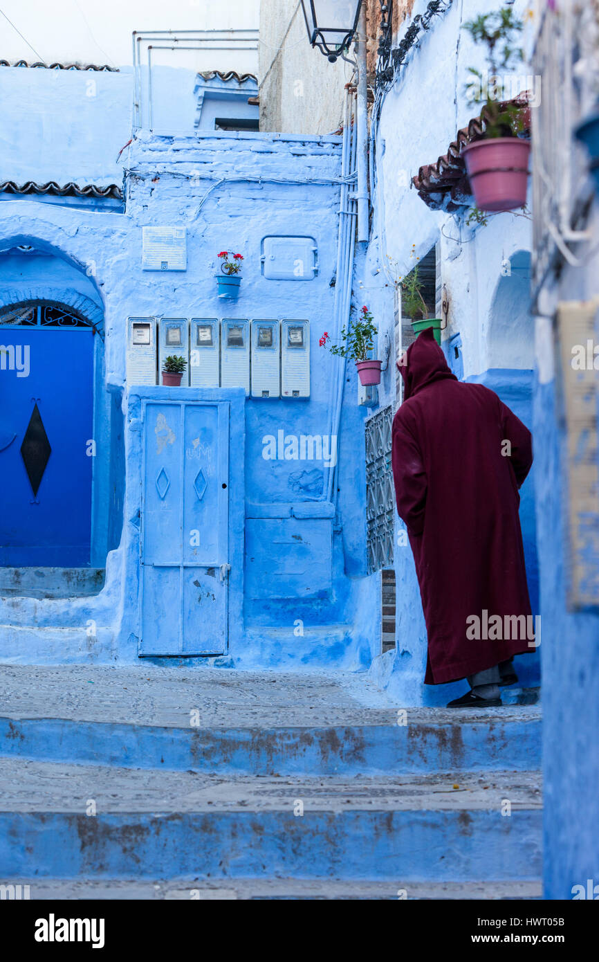 Chefchaouen, Morocco.  Man Standing in Entranceway to his House.  Neighborhood Electric Meters on wall in front. Stock Photo