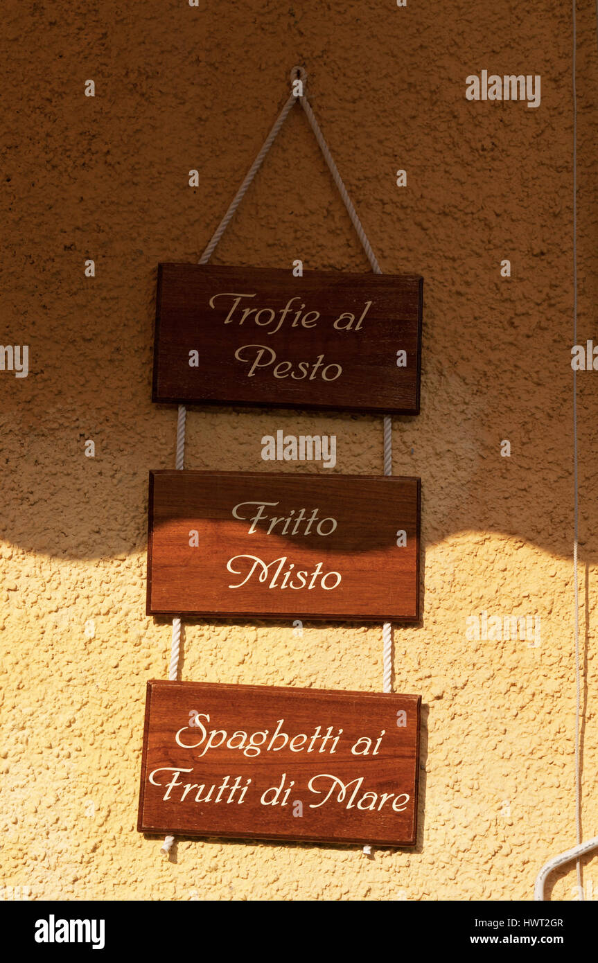 Wooden signs of trofie with pesto, stir-fry and seafood spaghetti hanging outside one of the restaurants in Piazzetta, the little square of Portofino Stock Photo