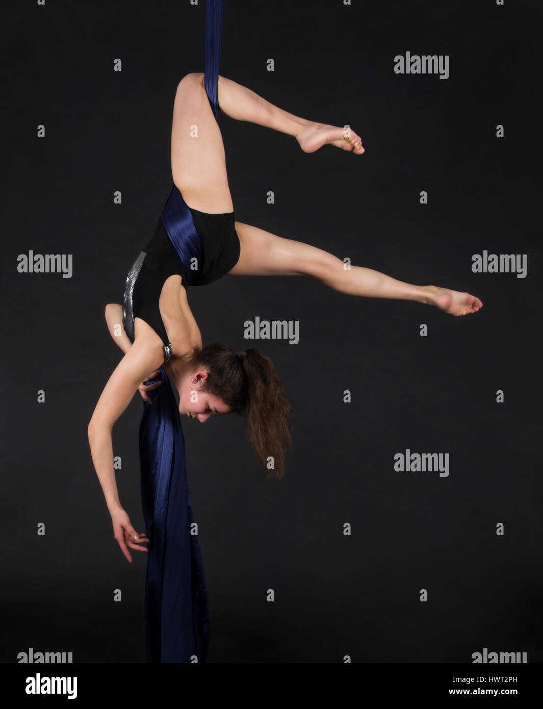Young, smiling woman does exercises on the canvases. Studio recording of the performance on a dark background. Stock Photo