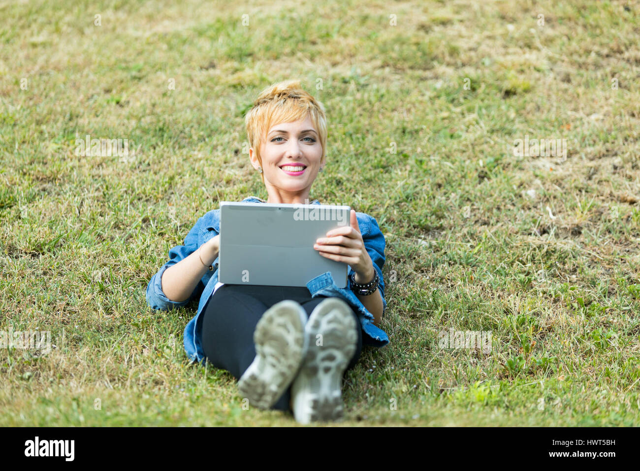 woman lying on a meadow with her digital tablet with wich she could make shopping or working on her e-comerce Stock Photo