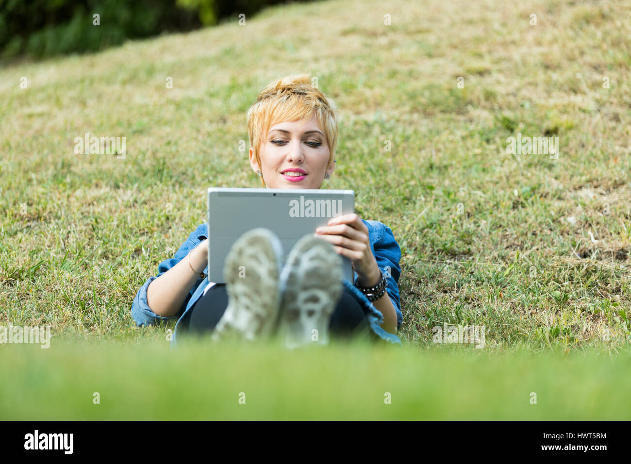 woman lying on a meadow with her digital tablet with wich she could make shopping or working on her e-comerce Stock Photo