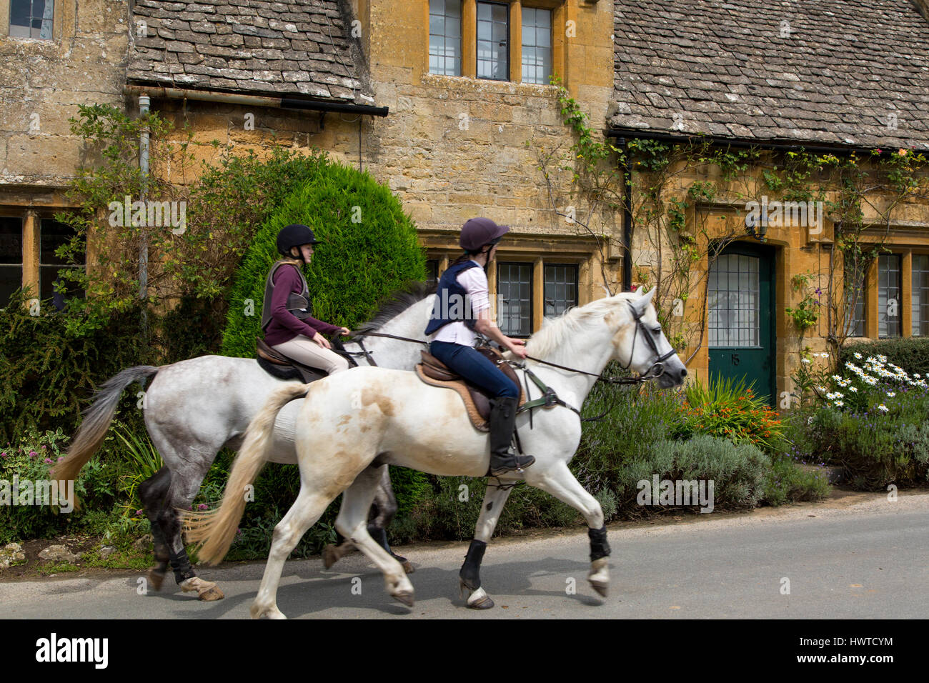 Riding horses through Cotswold village of Stanton,  Gloucestershire, England Stock Photo