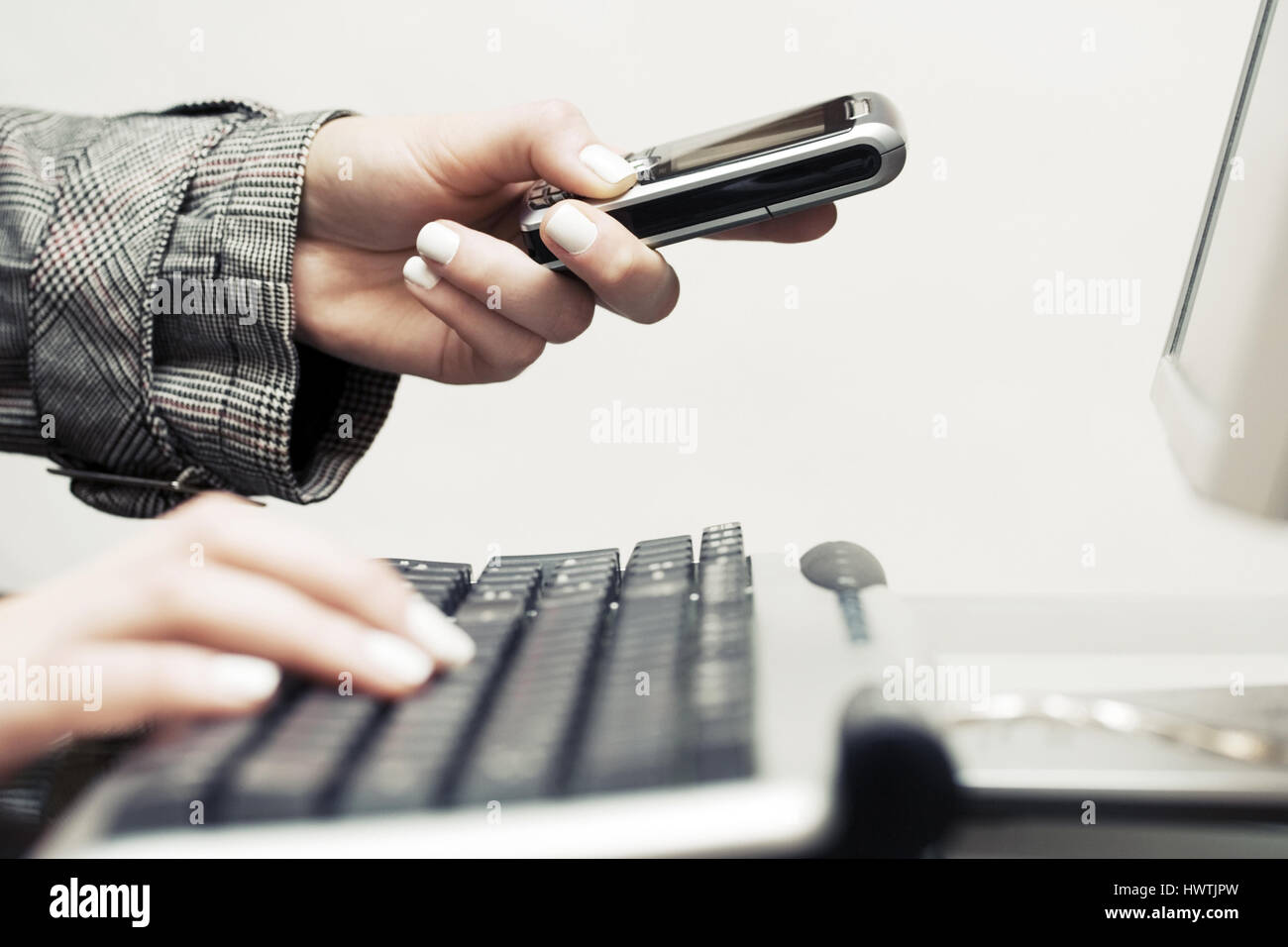Female hands typing on computer keyboard and calling on cell phone ...