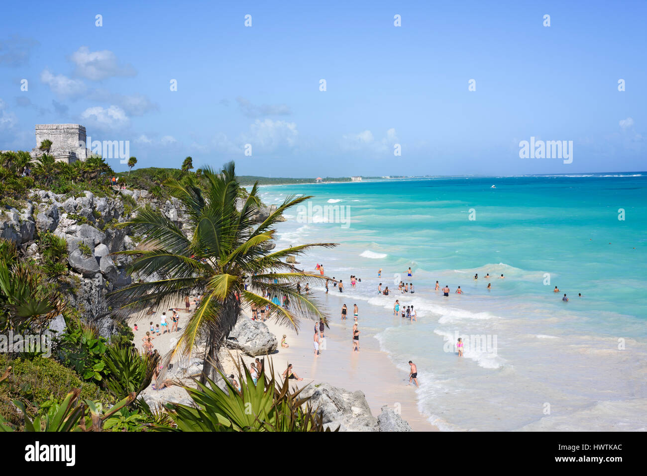Top view of the Caribbean Sea under blue sky, people having fun on beach in Tulum, Yucatan, Mexico, green tropical plant palm trees foreground Stock Photo