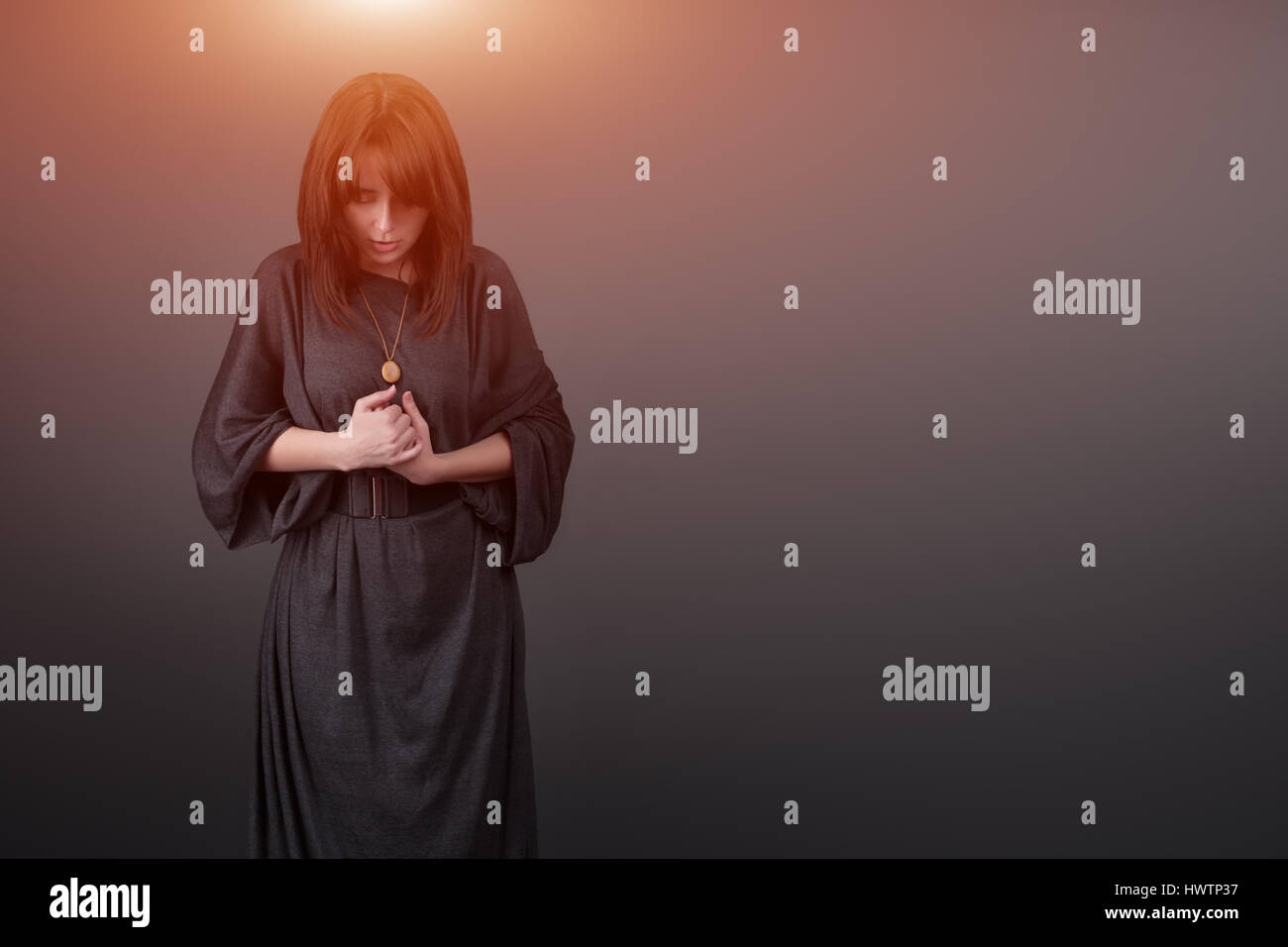Portrait of a young caucasian woman praying. Prayer girl dressed in Vestments of a nun on gray studio background. Religion and hope concept Stock Photo
