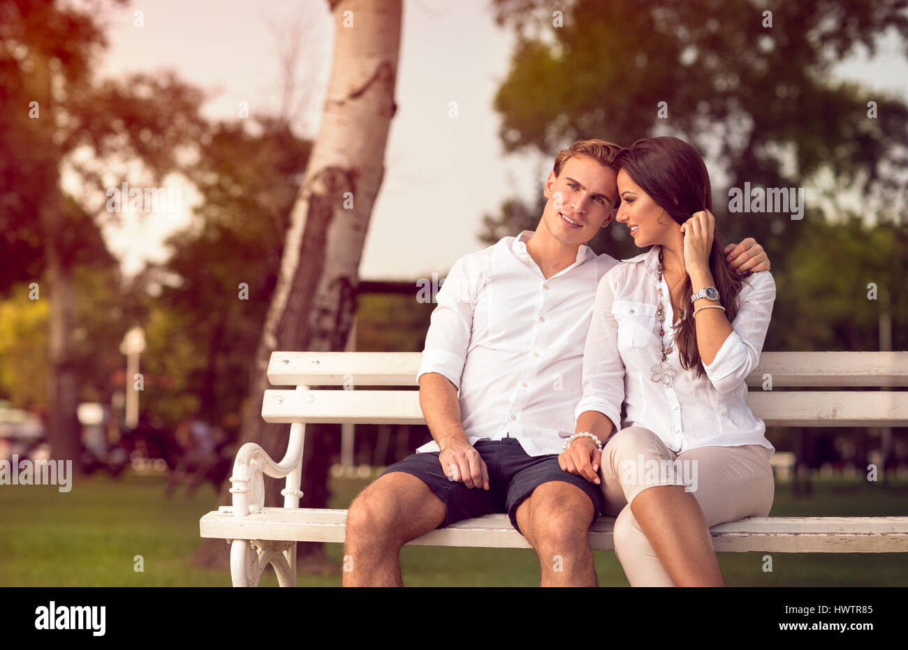 Cute young couple sitting at park on the bench Stock Photo - Alamy