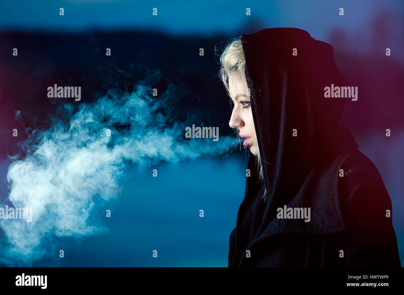 Young female exhaling smoke side shot in black Stock Photo
