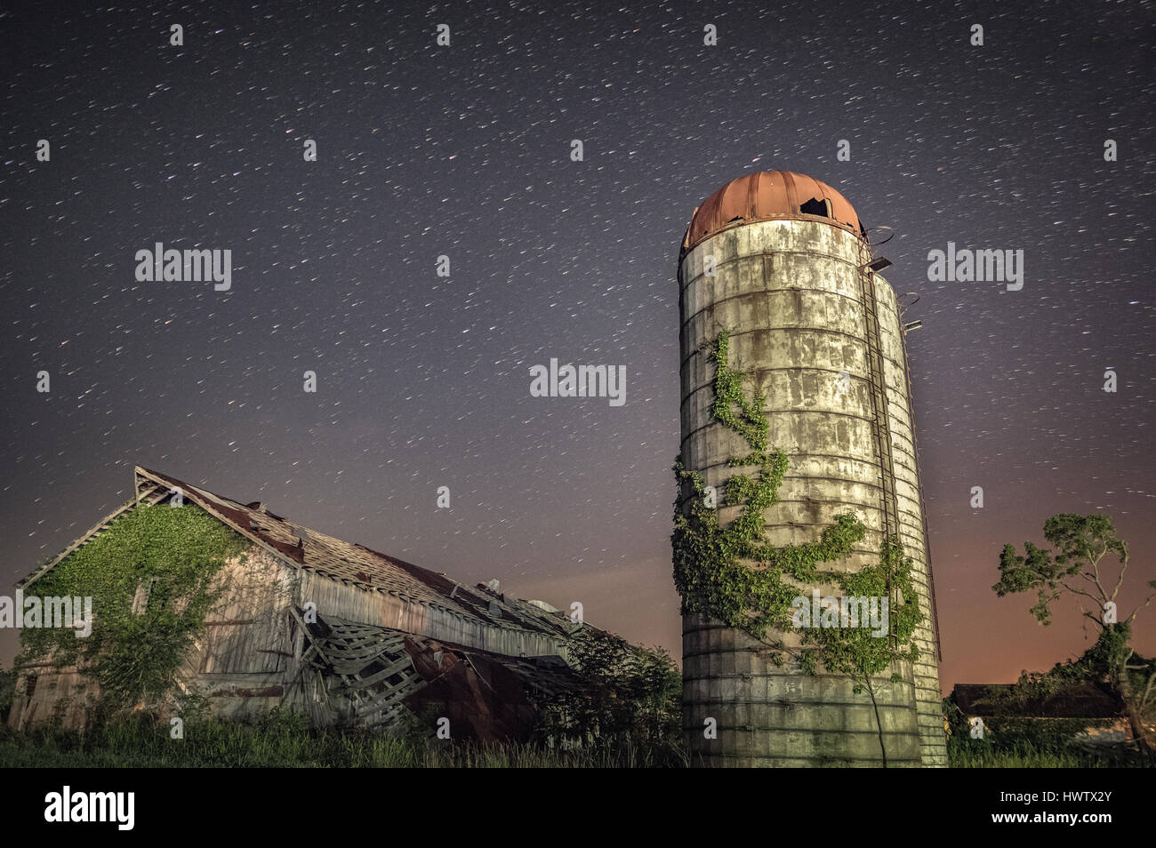 Among the encroaching environment, an old silo and barn stand in Mason County, West Virginia with a long exposure showing the movement of the stars. Stock Photo