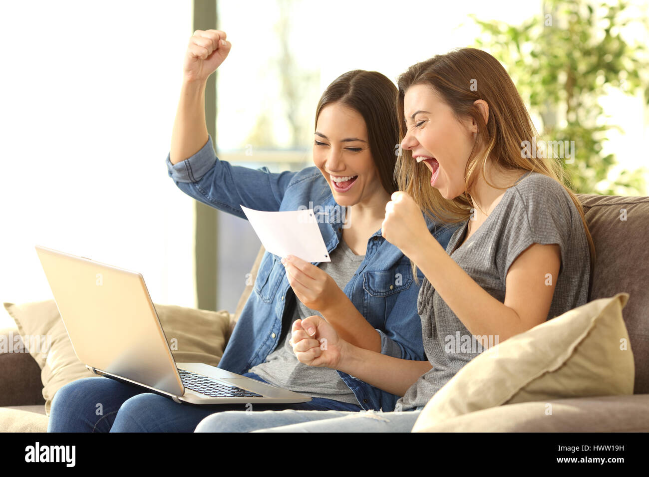 Excited roommates reading a bank notification sitting on a sofa in the living room at home Stock Photo