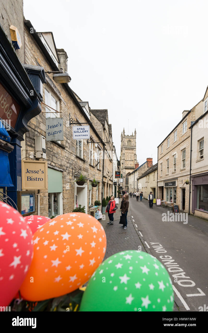 People walk down Black Jack Street with St John the Baptist parish church in the distance, Cirencester in the Cotswolds, Gloucester, England, UK Stock Photo