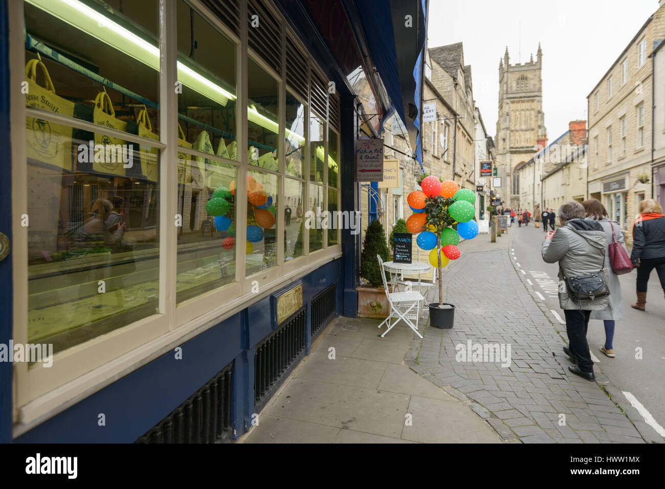 People walk down Black Jack Street with St John the Baptist parish church in the distance, Cirencester in the Cotswolds, Gloucester, England, UK Stock Photo