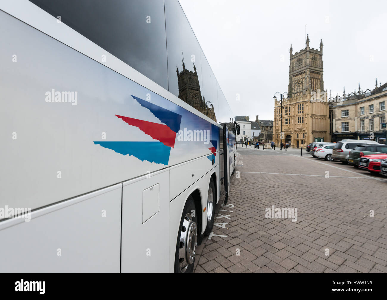 A holiday coach parks on Market Street with St John the Baptist parish church behind, Cirencester in the Cotswolds, Gloucester, England, UK Stock Photo