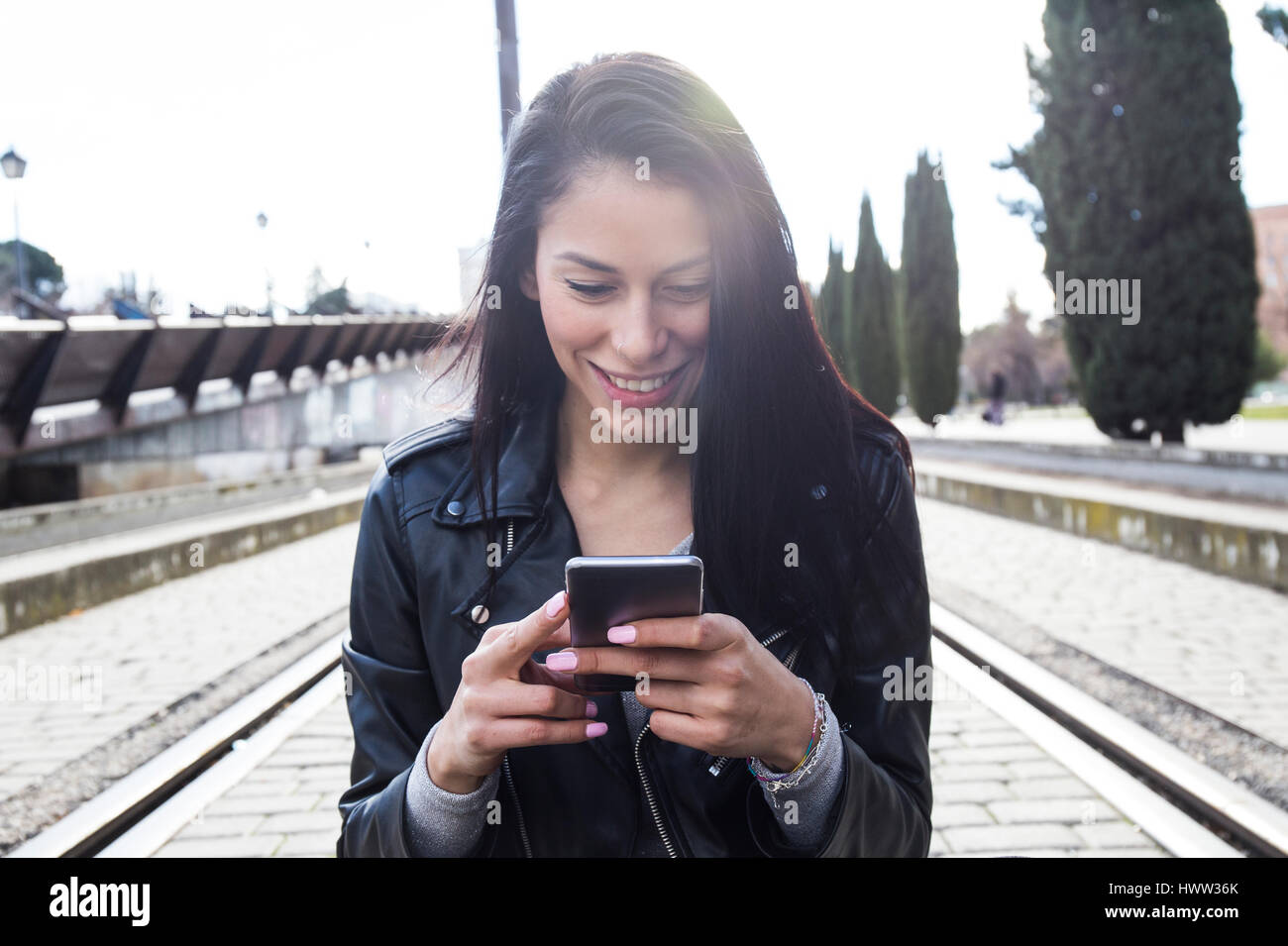 Portrait of smiling young woman  wearing black leather jacket looking at cell phone Stock Photo