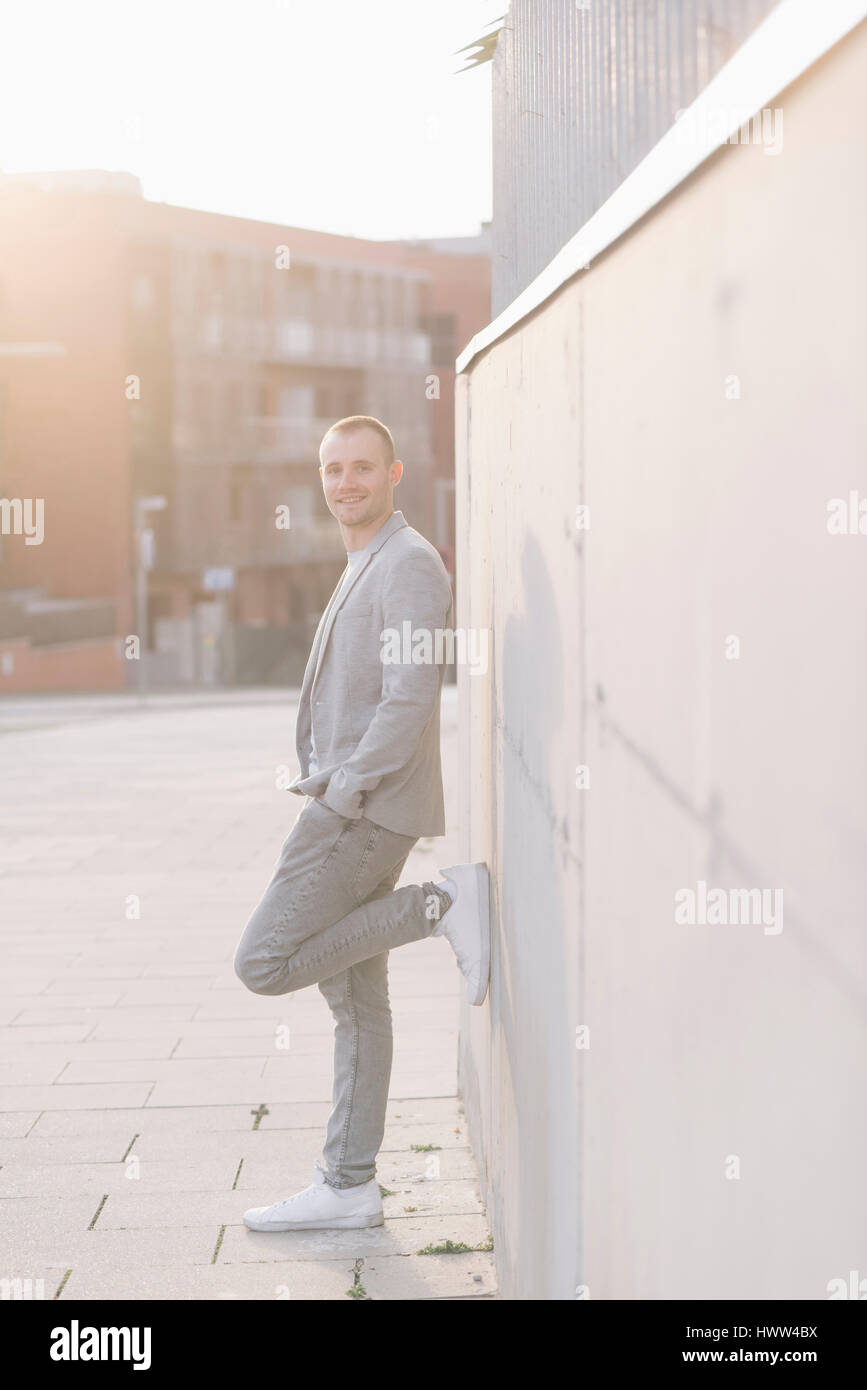 Smiling man leaning against a wall at backlight Stock Photo - Alamy