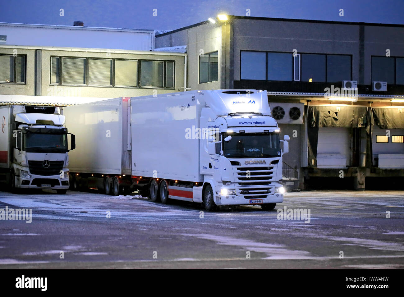 SALO, FINLAND - NOVEMBER 27, 2016: Big white refrigerated trailer truck ready to unload at warehause in winter evening snowfall. Stock Photo