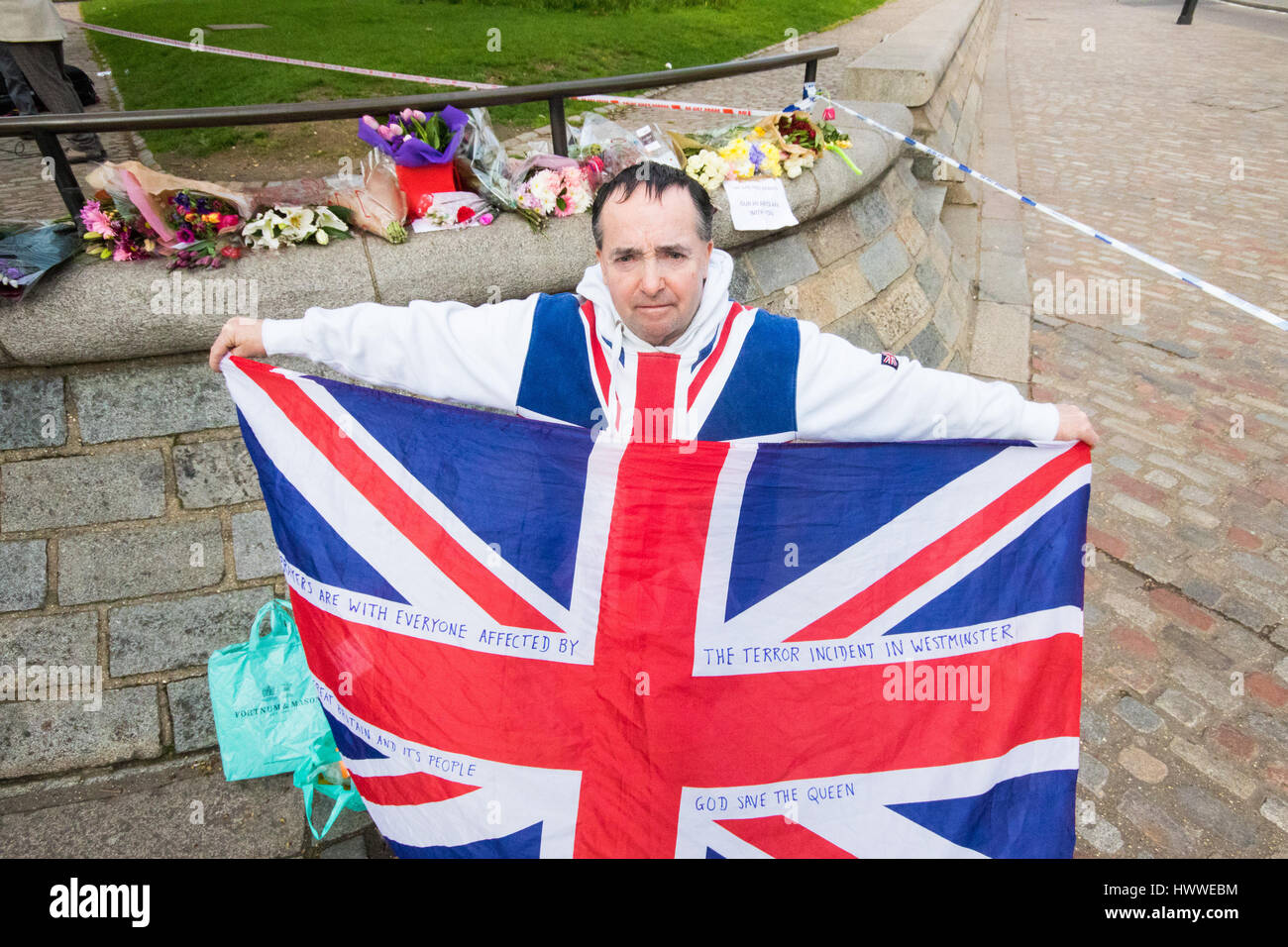 Westminster, London, UK. 23rd Mar, 2017. With his flag and a bunch of roses, John Loughrey of Streatham mourns those killed and injured in Tuesday's terrorist attack on Westminster Bridge and in the grounds of Parliament, in which three people and their attacker were killed with over 40 injured. Credit: Paul Davey/Alamy Live News Stock Photo